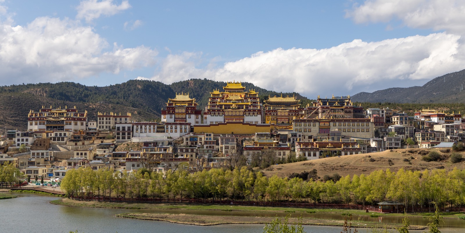 松赞林寺全景：藏式寺院群坐落高原，背后群山与云天